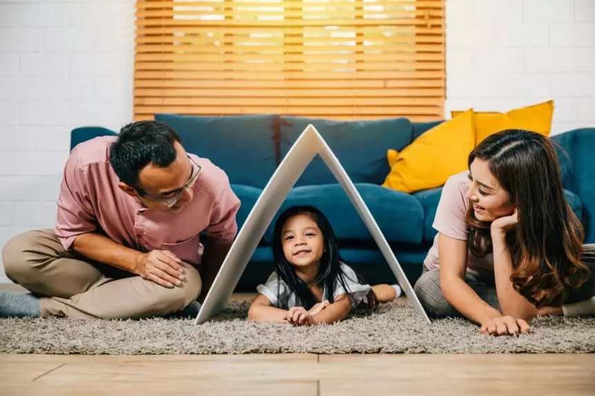 A portrait of a harmonious family sitting on a couch holding a cardboard roof