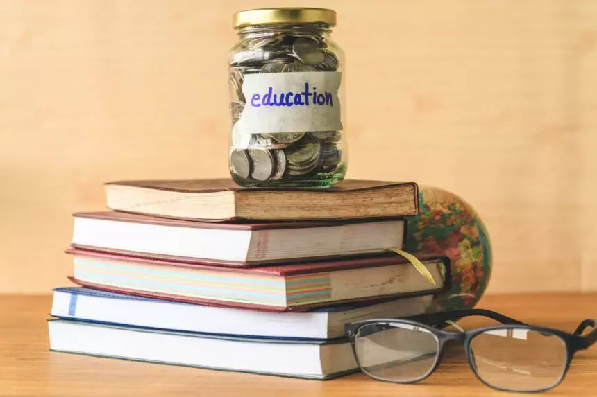 Coins in glass jar with education label, books,glasses and globe on wooden table. Financial concept.
