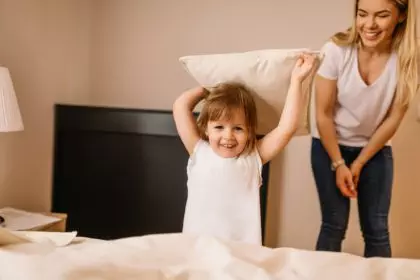 Happy child with parents having pillow fight in bed at home